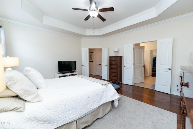 bedroom featuring a tray ceiling, wood finished floors, baseboards, and ornamental molding