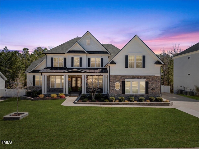 view of front of house featuring fence, a lawn, stone siding, driveway, and a standing seam roof