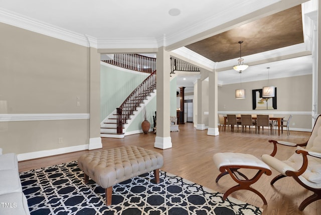 interior space featuring wood finished floors, baseboards, ornate columns, stairs, and crown molding