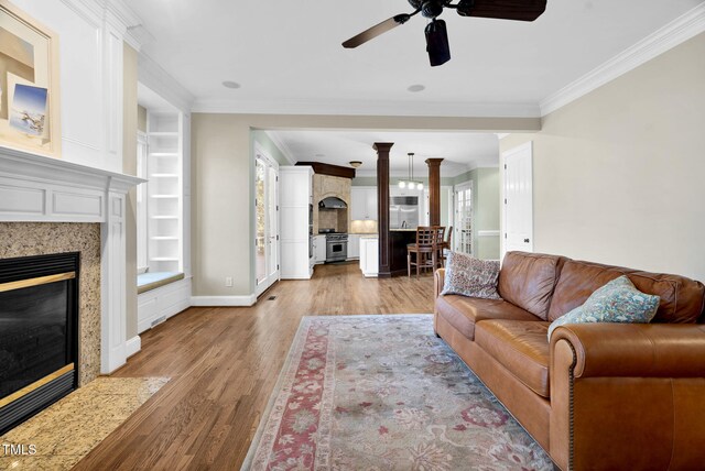 living area featuring built in features, a ceiling fan, light wood-style flooring, a fireplace, and crown molding