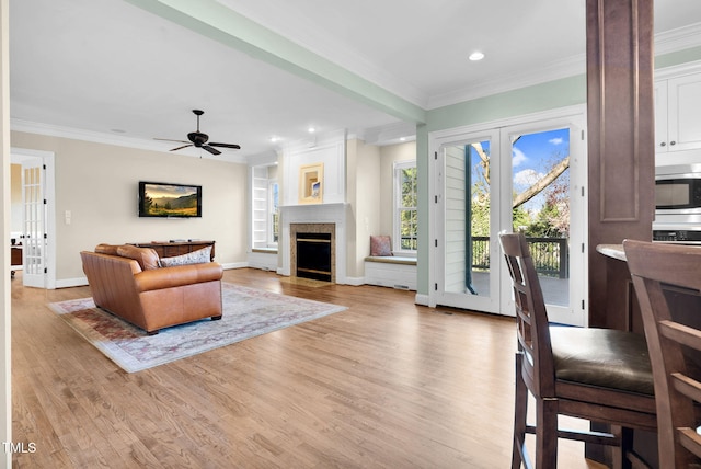 living area with a ceiling fan, a fireplace, ornamental molding, french doors, and light wood-type flooring