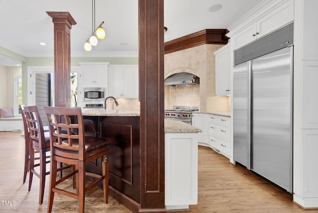 kitchen with ornamental molding, white cabinetry, light wood finished floors, decorative columns, and built in appliances