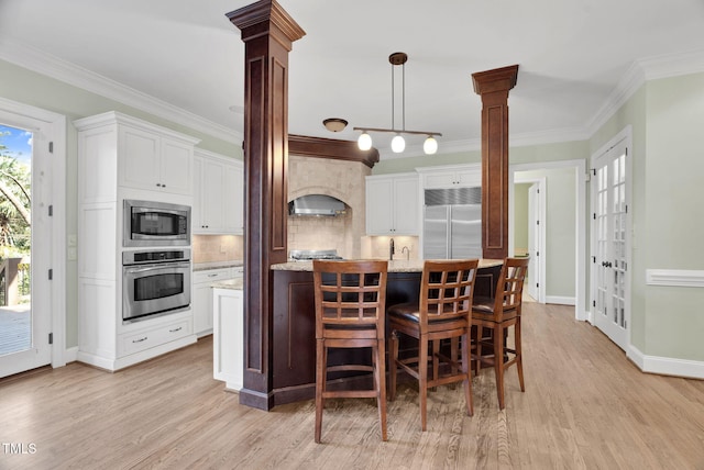 kitchen featuring crown molding, decorative columns, light wood-style floors, and built in appliances