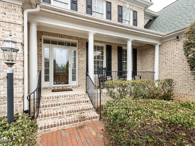 doorway to property featuring a porch and a shingled roof