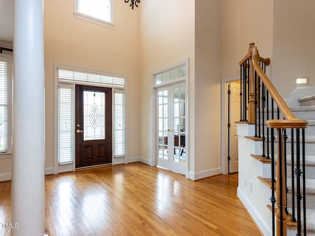 entryway featuring baseboards, decorative columns, stairs, light wood-style floors, and french doors