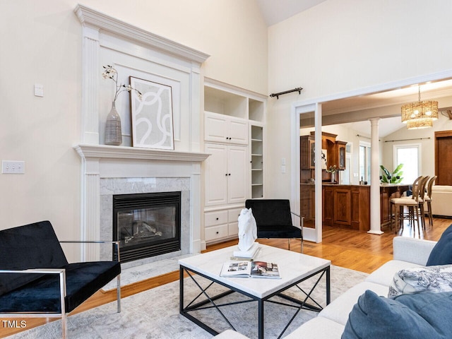 living area featuring wood finished floors, ornate columns, high vaulted ceiling, an inviting chandelier, and a high end fireplace