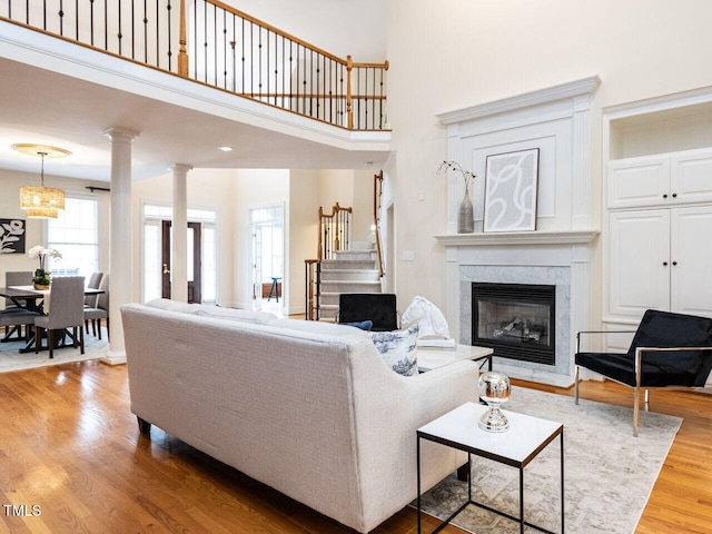 living room featuring wood finished floors, stairway, a fireplace, a towering ceiling, and ornate columns