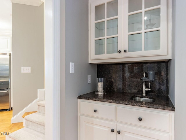 bar with tasteful backsplash, stainless steel built in refrigerator, wet bar, wood finished floors, and a sink