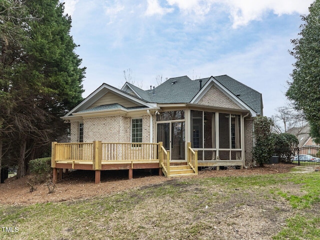 back of house with brick siding, roof with shingles, a deck, and a sunroom