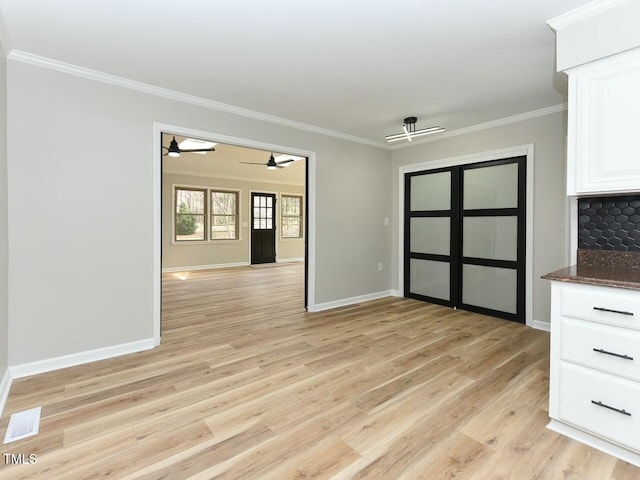 unfurnished dining area with visible vents, light wood-style flooring, a ceiling fan, crown molding, and baseboards