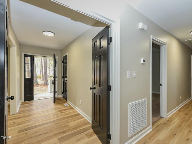 hallway featuring light wood-style floors, visible vents, and baseboards