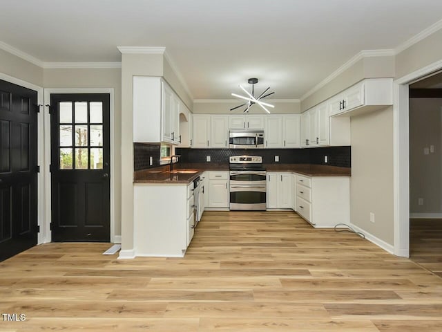 kitchen with a notable chandelier, a sink, dark countertops, appliances with stainless steel finishes, and light wood finished floors