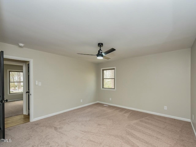 carpeted spare room with a healthy amount of sunlight, baseboards, and ceiling fan