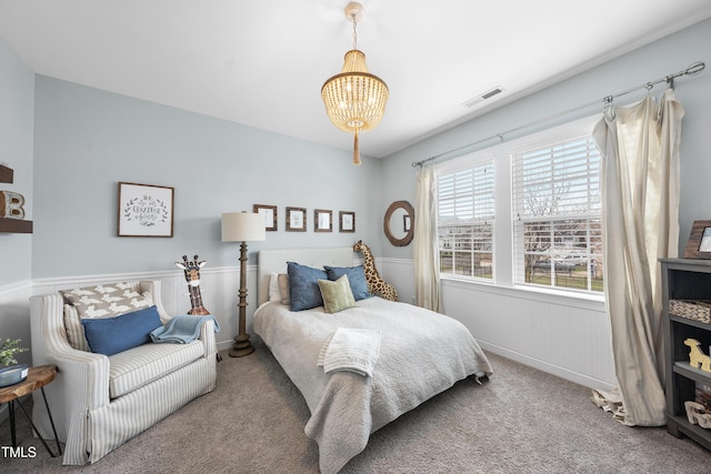 carpeted bedroom featuring an inviting chandelier, visible vents, and wainscoting