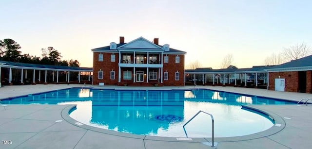 pool at dusk with a patio and a community pool