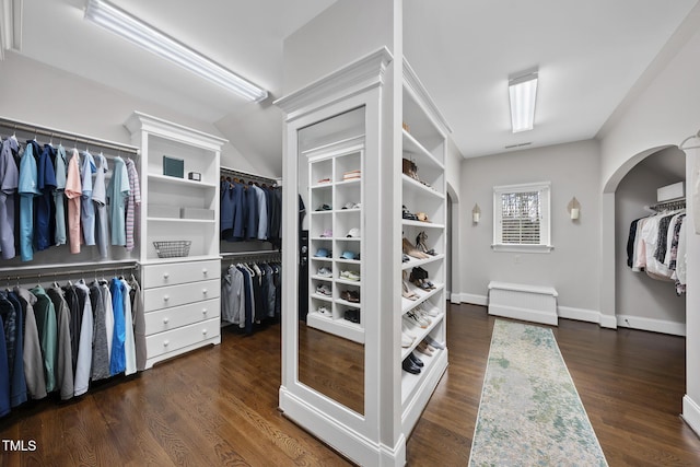 spacious closet with arched walkways and dark wood-style flooring