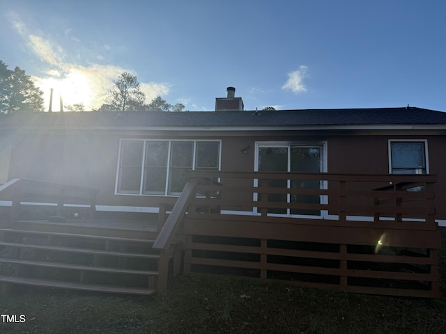 rear view of property with roof with shingles, a deck, and a chimney