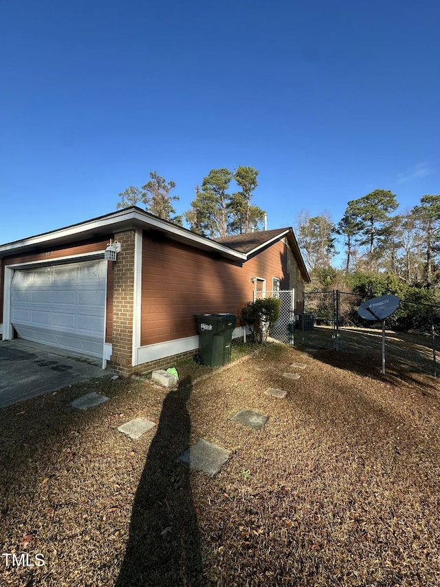 view of side of property featuring brick siding, an attached garage, and fence