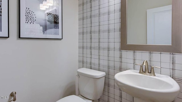 half bathroom featuring backsplash, toilet, tile walls, and a sink