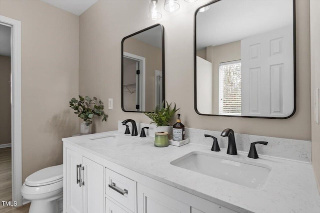 bathroom with double vanity, toilet, and a sink