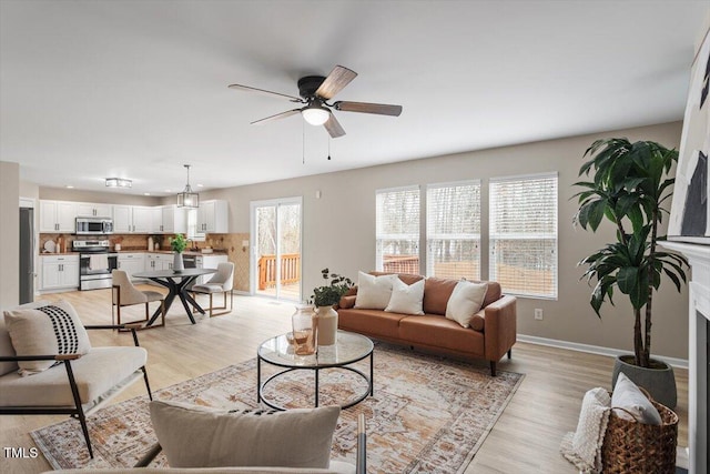 living area featuring light wood-style flooring, baseboards, and a ceiling fan