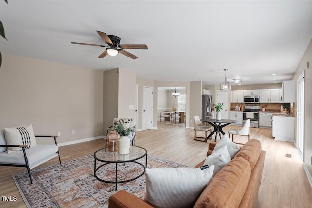 living area with light wood-style flooring, ceiling fan with notable chandelier, and baseboards