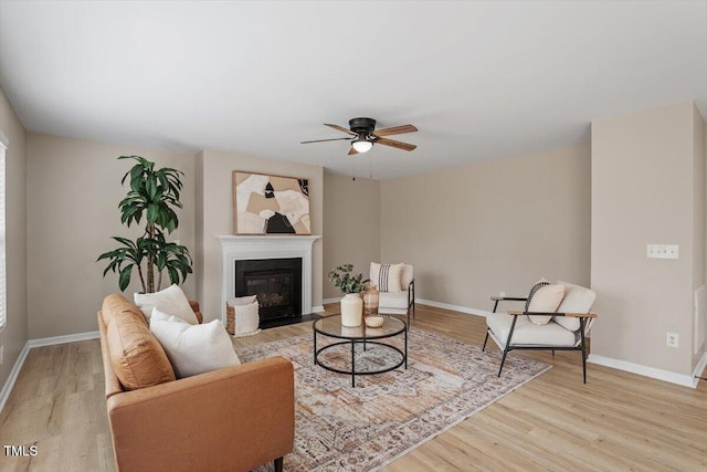 living room featuring a fireplace with flush hearth, light wood-style flooring, a ceiling fan, and baseboards