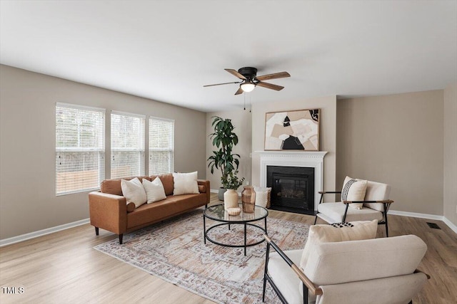 living area featuring a glass covered fireplace, baseboards, and wood finished floors