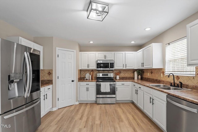 kitchen featuring backsplash, light wood-style flooring, stainless steel appliances, white cabinetry, and a sink