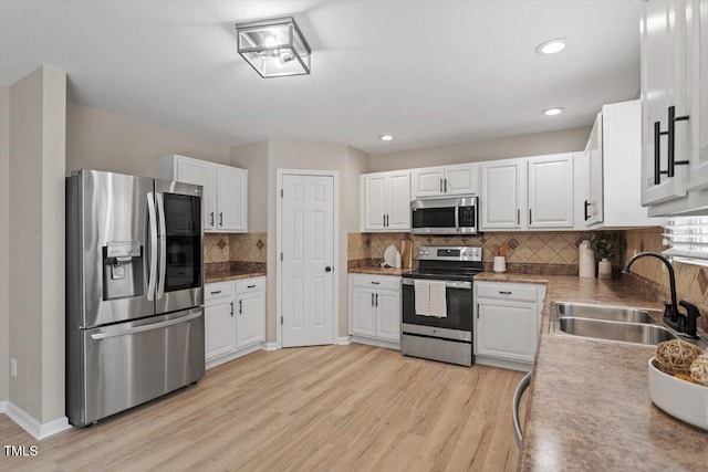 kitchen with a sink, tasteful backsplash, stainless steel appliances, light wood-style floors, and white cabinets