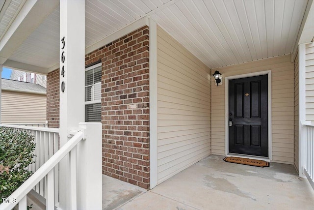 view of exterior entry with brick siding and covered porch