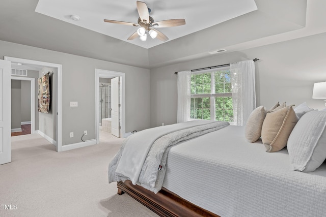 bedroom with visible vents, baseboards, light colored carpet, a tray ceiling, and a ceiling fan