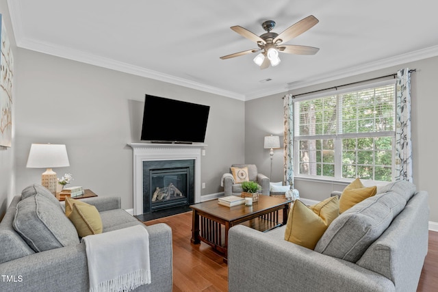 living room featuring a fireplace with flush hearth, crown molding, a ceiling fan, and wood finished floors