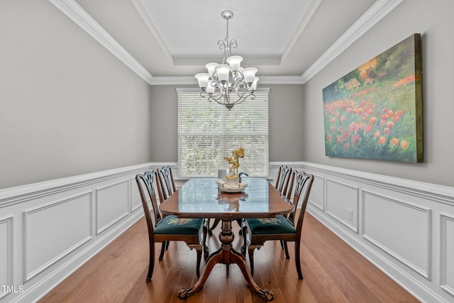 dining space featuring a raised ceiling, wainscoting, light wood finished floors, and a chandelier