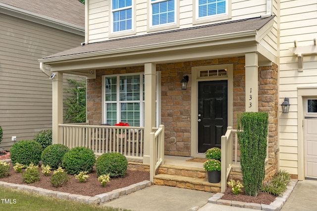 view of exterior entry with stone siding, a porch, and roof with shingles