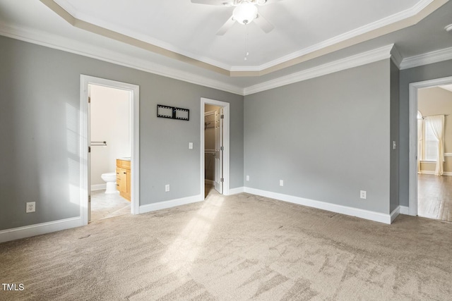 unfurnished bedroom with carpet, baseboards, ensuite bath, ornamental molding, and a walk in closet