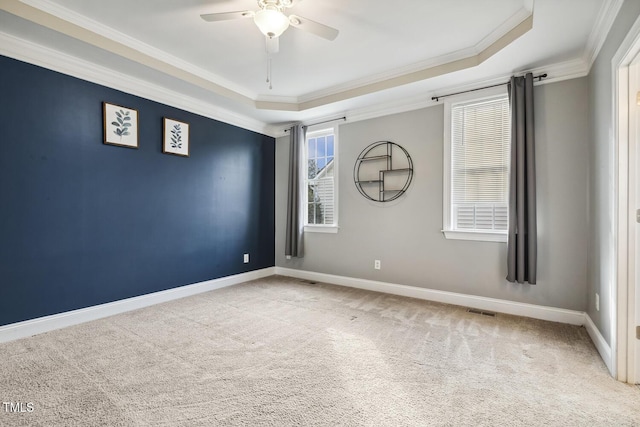 carpeted empty room with visible vents, a raised ceiling, baseboards, and ornamental molding