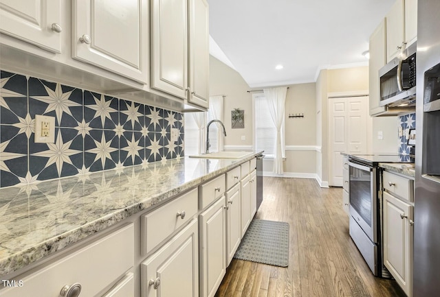 kitchen with decorative backsplash, wood finished floors, appliances with stainless steel finishes, and a sink