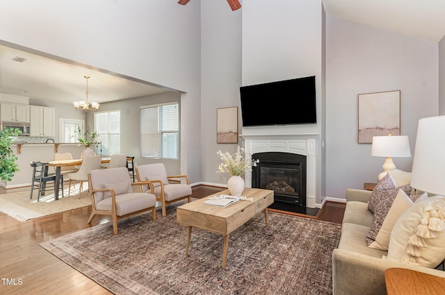 living room with visible vents, baseboards, a towering ceiling, wood finished floors, and a glass covered fireplace