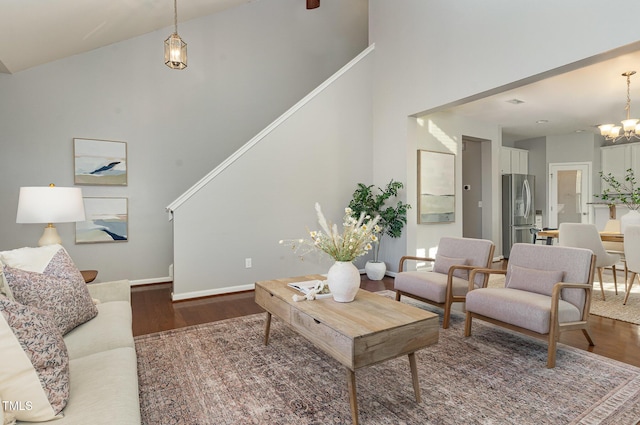 living area featuring baseboards, high vaulted ceiling, an inviting chandelier, and wood finished floors