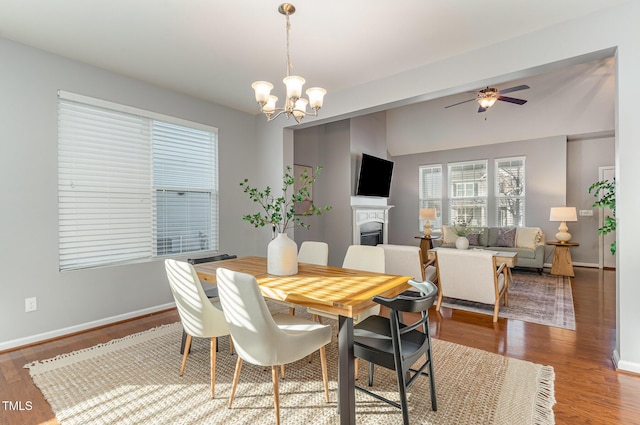 dining space featuring ceiling fan with notable chandelier, a fireplace, baseboards, and wood finished floors