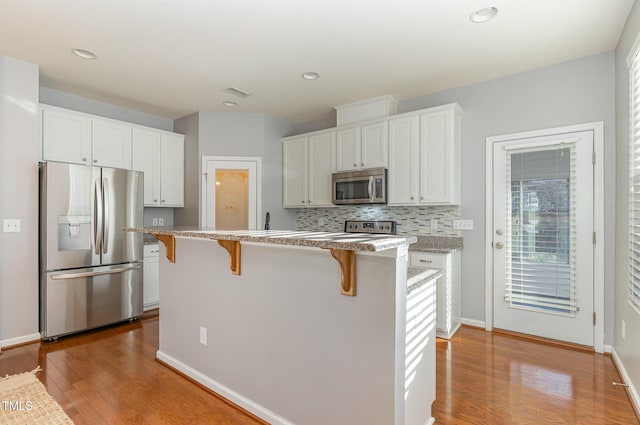 kitchen featuring a breakfast bar, white cabinetry, stainless steel appliances, and tasteful backsplash