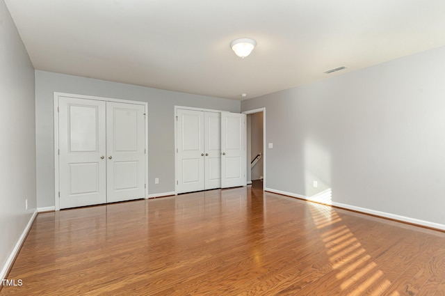 unfurnished bedroom featuring visible vents, wood finished floors, multiple closets, and baseboards