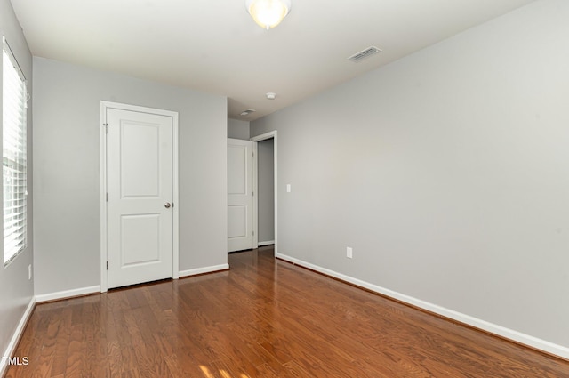 unfurnished bedroom featuring multiple windows, wood finished floors, visible vents, and baseboards