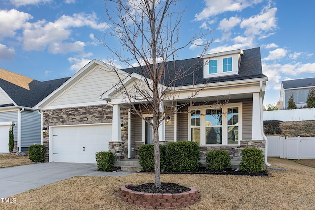 craftsman-style house featuring fence, a porch, an attached garage, concrete driveway, and stone siding