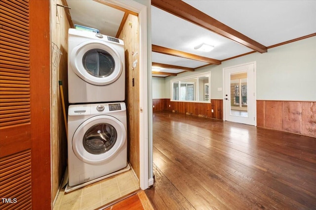 laundry area with a wainscoted wall, stacked washing maching and dryer, wood-type flooring, wood walls, and laundry area