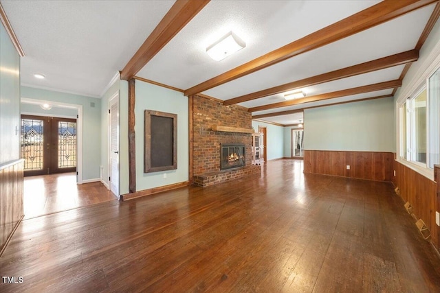 unfurnished living room with a wainscoted wall, beam ceiling, wood-type flooring, and french doors