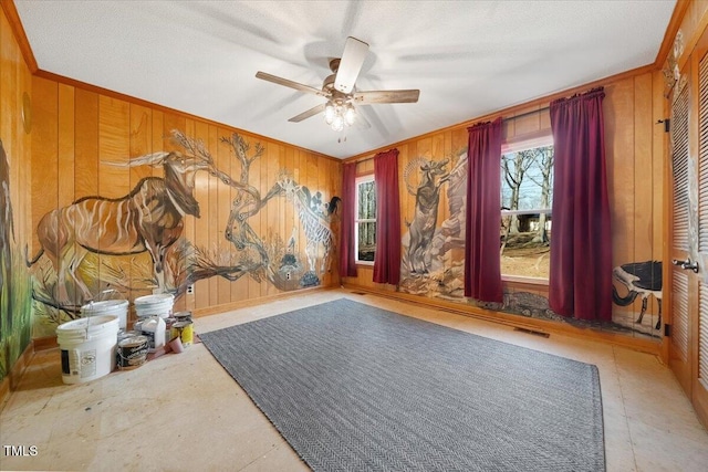 interior space featuring ceiling fan, visible vents, wood walls, and ornamental molding