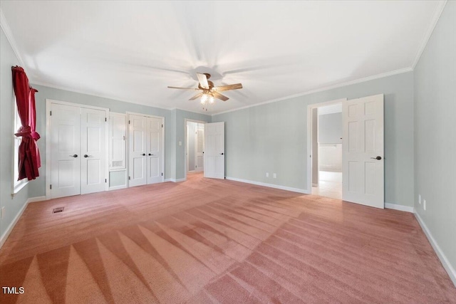 unfurnished bedroom featuring light colored carpet, baseboards, crown molding, and multiple closets