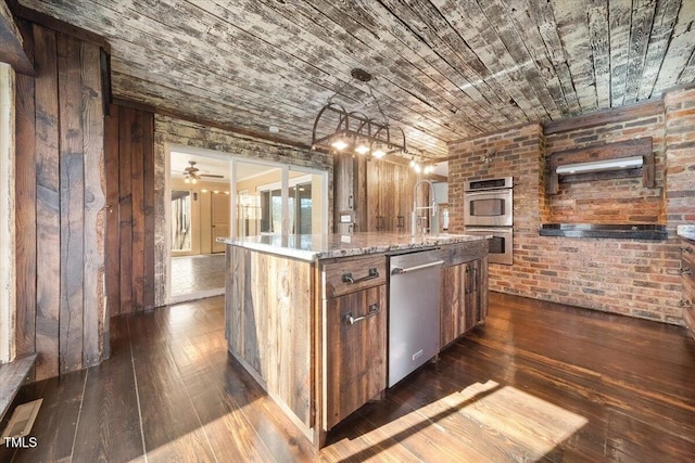 kitchen with brown cabinets, a center island with sink, dark wood finished floors, appliances with stainless steel finishes, and brick wall